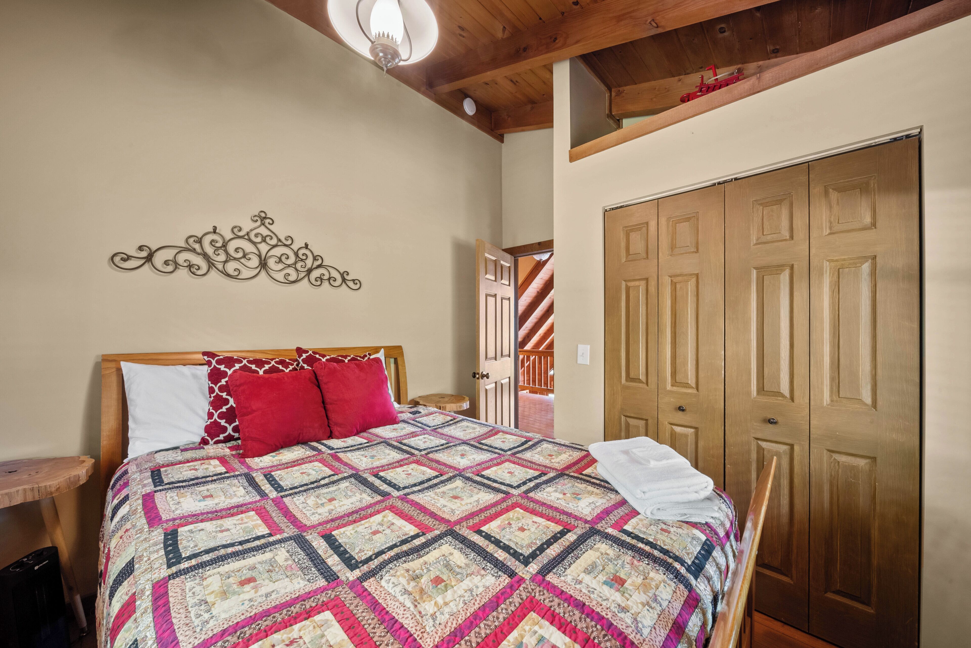 A bedroom with a wooden bed, a quilt, a nightstand, a wardrobe, and a staircase.