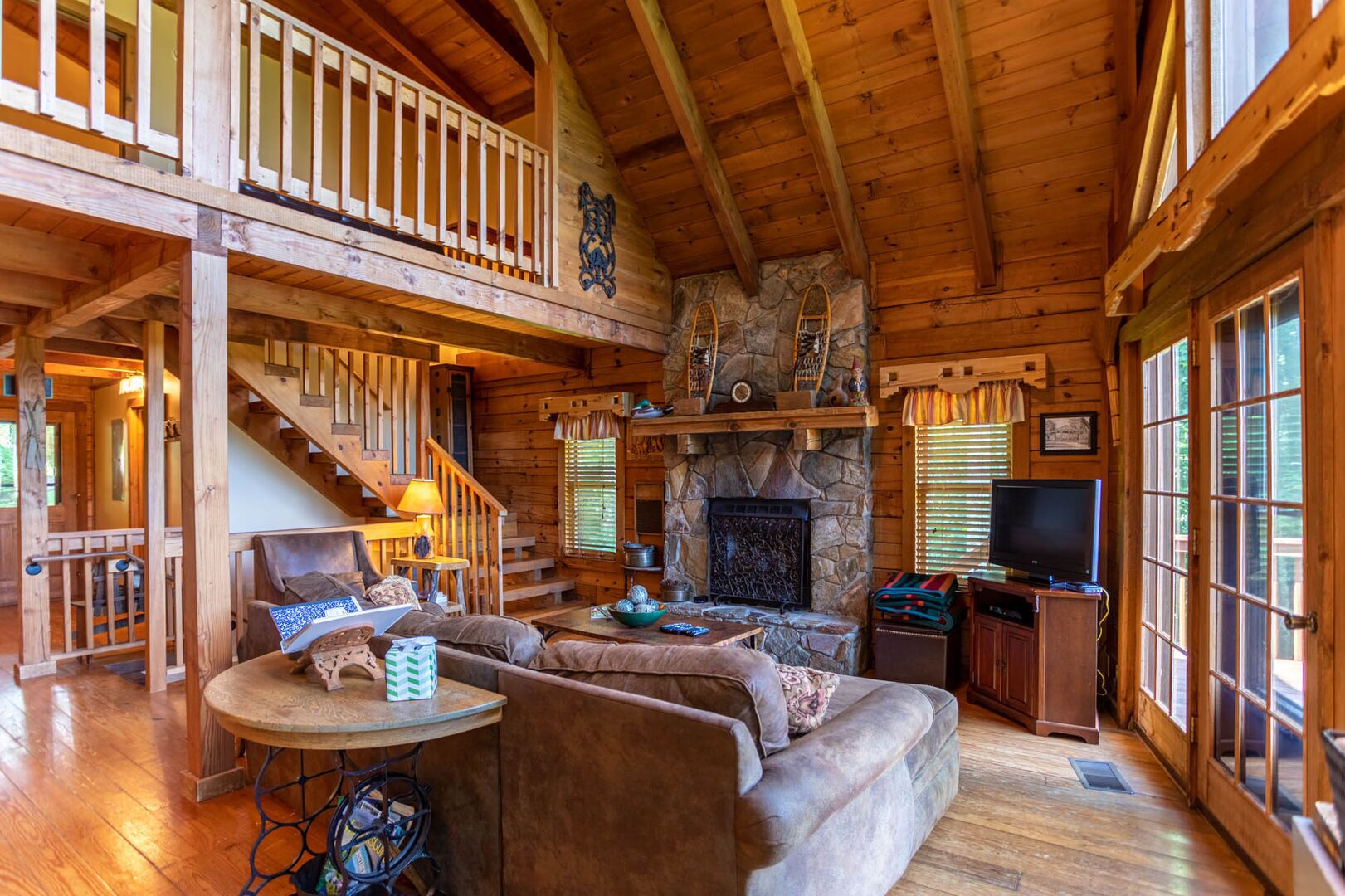 A cozy cabin interior with a stone fireplace, wooden furniture, and a balcony.