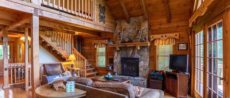 A cozy cabin interior with a stone fireplace, wooden furniture, and a balcony.