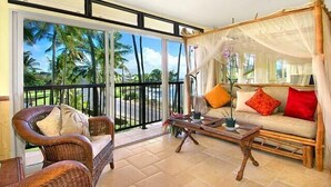 A room with a balcony, wicker furniture, a canopy bed, and a view of palm trees. - Fabulous condo, great ocean views, steps from a great snorkeling beach. (Poipu)