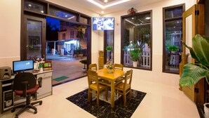 A hotel lobby with a reception desk, a dining area with a table and chairs, and large windows offering views of the street outside. - Quynh Chau Homestay (Da Nang)