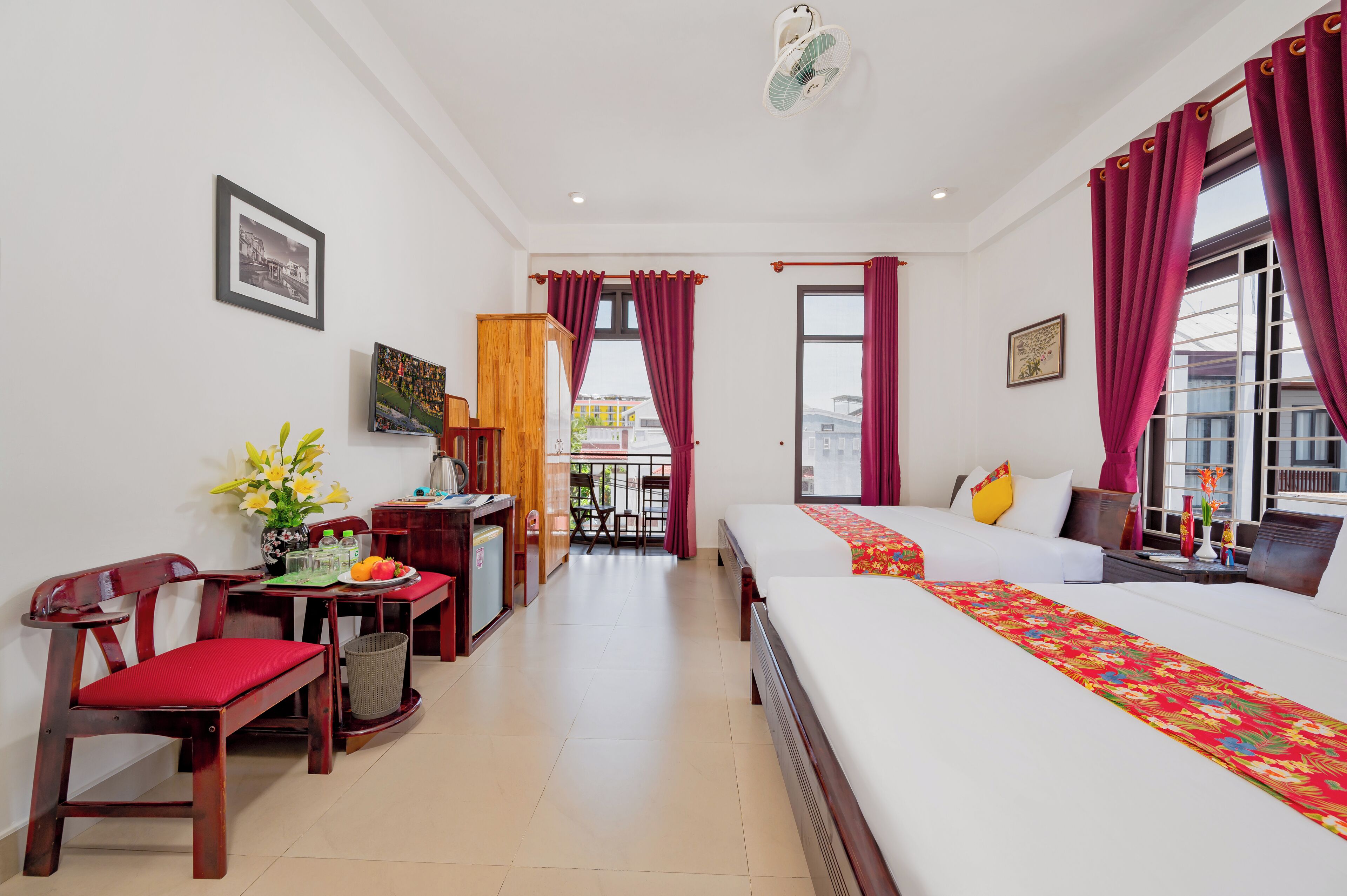 A hotel room with a bed, a desk with a chair, a small table with a vase of flowers, and a balcony with a view.