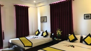 A hotel room with two beds, each with a yellow and black bedspread, and red curtains. There is a small table with a vase of flowers and a framed picture on the wall. - Quynh Chau Homestay (Da Nang)
