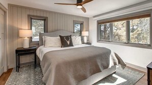 A bedroom with a bed, two nightstands, a ceiling fan, and large windows.