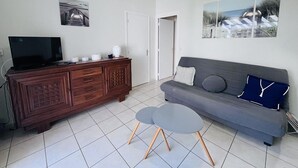 A living room with a TV, wooden cabinet, grey sofa, two small tables, and artwork on the walls. - Terraced villa in front of the sporting casino (HOSSEGOR)