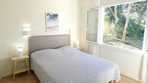 A bedroom with a bed, bedside lamps, a window with a view of trees, and a wall-mounted picture. - Terraced villa in front of the sporting casino (HOSSEGOR)