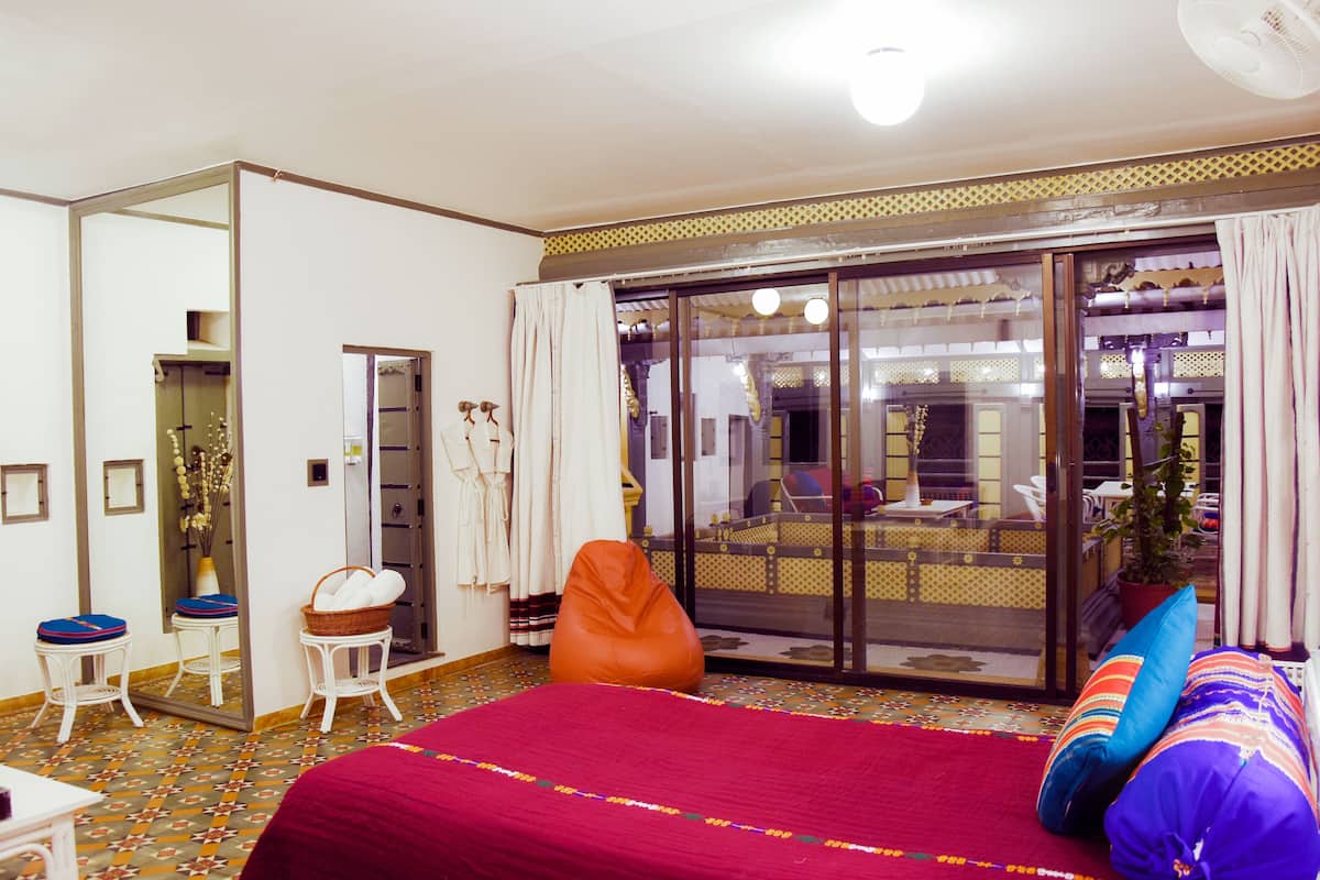 Ein Hotelzimmer mit einem großen Bett, einer Sitzecke mit einem Sessel und einem kleinen Tisch, einem großen Fenster mit Vorhängen und einer Glastür zum Balkon.