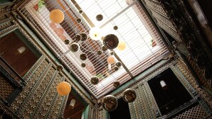 Un intérieur richement décoré, avec un plafond haut, des éléments de ferronnerie complexes et une série de luminaires sphériques.