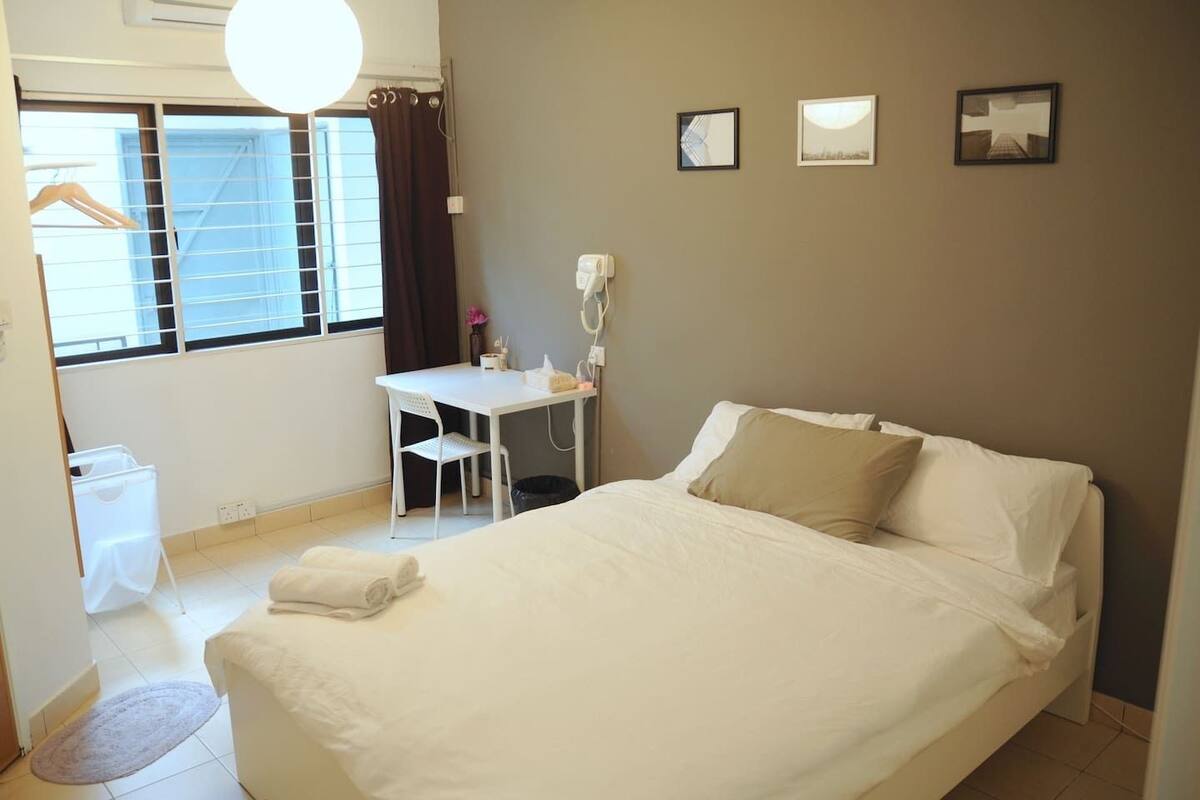 A hotel room with a large bed, a desk with a chair, a telephone, and a window with curtains.