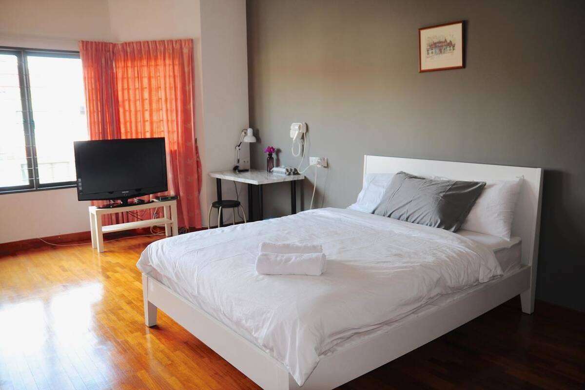 A hotel room with a bed, a TV on a stand, a desk with a lamp, and a window with curtains.