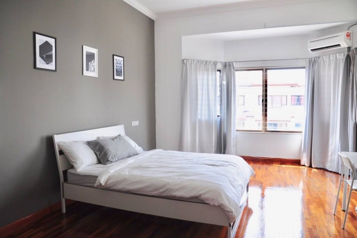 A modern bedroom with a white bed, grey walls, and a large window with curtains.
