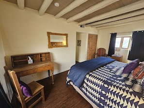 Een slaapkamer met een houten bureau, een bed met beddengoed met een patroon, een spiegel en een raam met gordijnen.