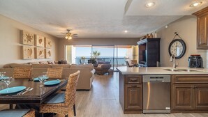 A modern kitchen with a central island, a dining area with wicker chairs, and a view of the ocean.