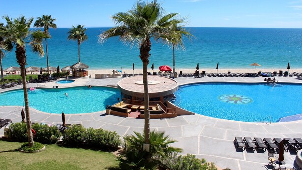 A resort with a large pool, palm trees, and a view of the ocean.