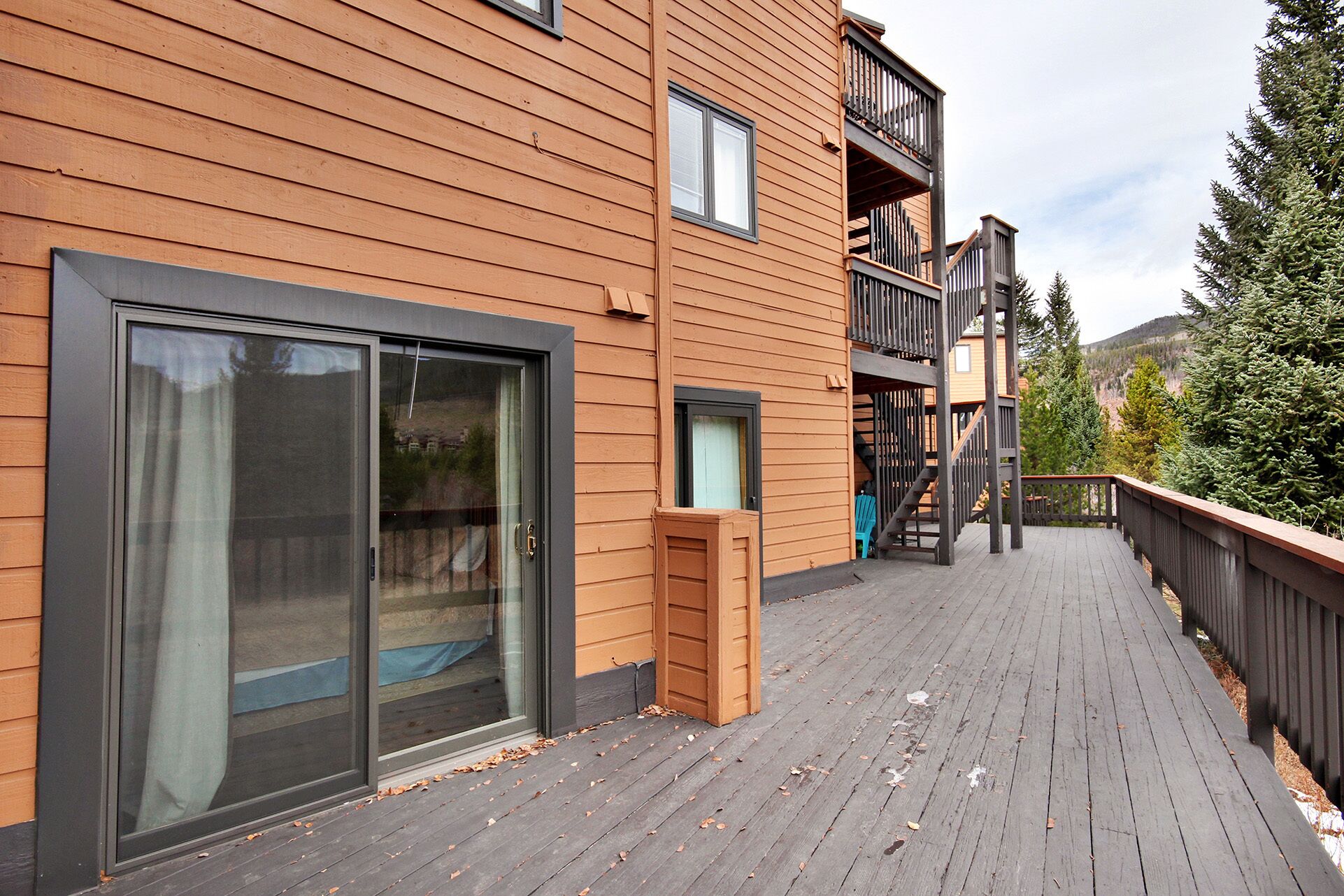A wooden building with a deck, large sliding glass doors, and a staircase leading to a balcony.