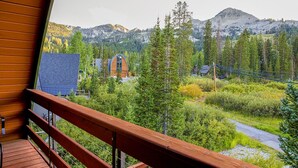 Un balcón de madera con vistas a un paisaje montañoso, que incluye una cabaña y un edificio azul.