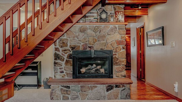 Una chimenea de piedra con repisa, una escalera de madera y un muro de piedra.