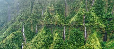 A lush, mountainous landscape with multiple waterfalls cascading down the slopes.