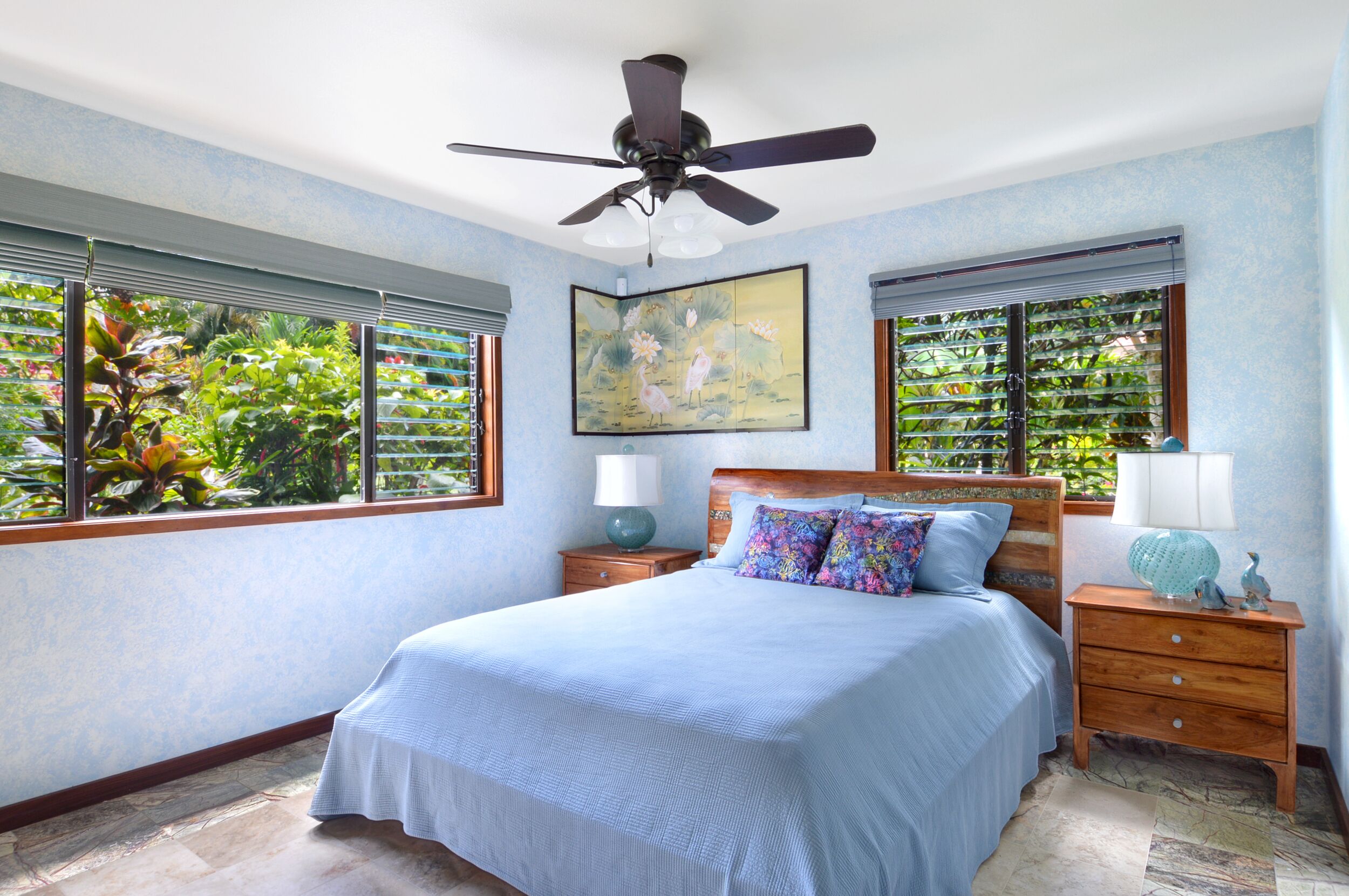 A bedroom with a bed, nightstands, a ceiling fan, and windows with blinds.