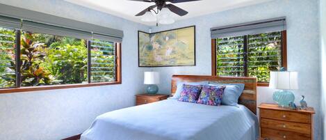 A bedroom with a bed, nightstands, a ceiling fan, and windows with blinds.