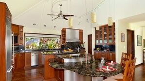 Une cuisine moderne dotée d’un îlot central, de meubles en bois, d’appareils électroménagers en acier inoxydable et de luminaires suspendus.