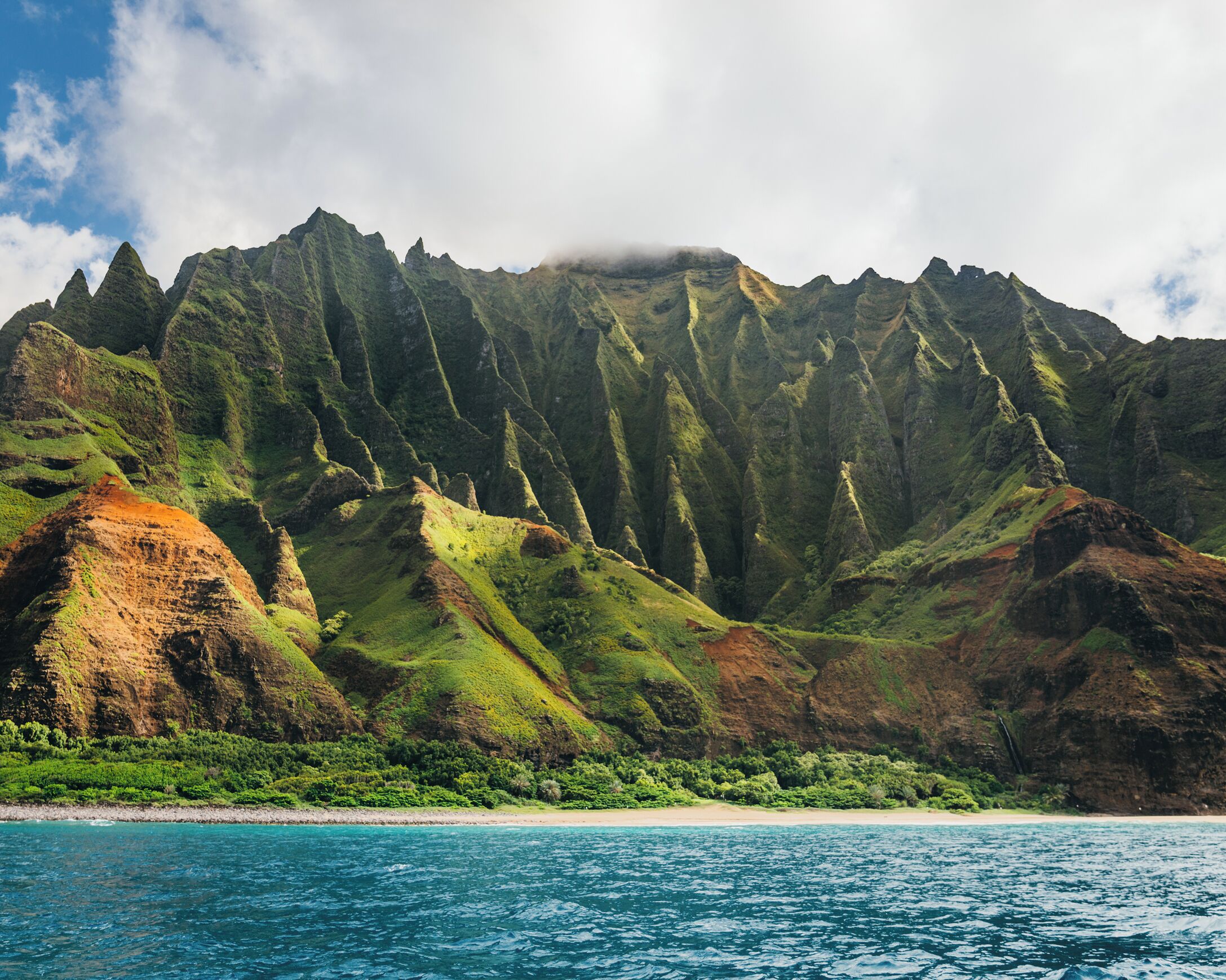A coastal landscape with a mountain range, a beach, and clear blue waters.