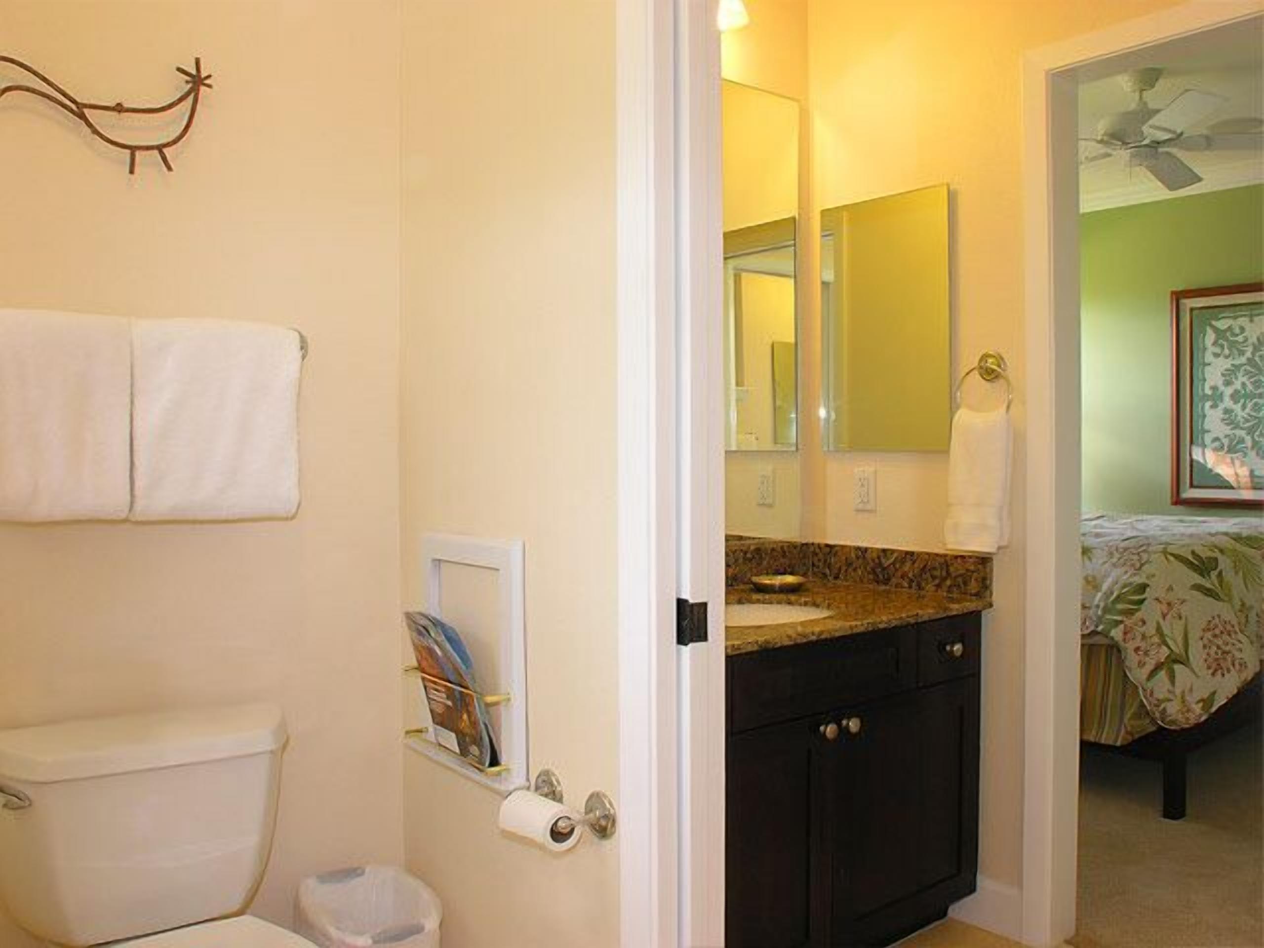 Un baño con inodoro, toallero, espejo y lavabo con un mueble oscuro.