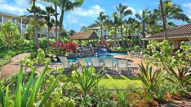 Ein Poolbereich eines Resorts mit Liegestühlen, Palmen und einer kleinen Laube.