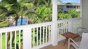 Ein überdachter Balkon mit Blick auf ein Schwimmbecken und üppige tropische Bepflanzung.