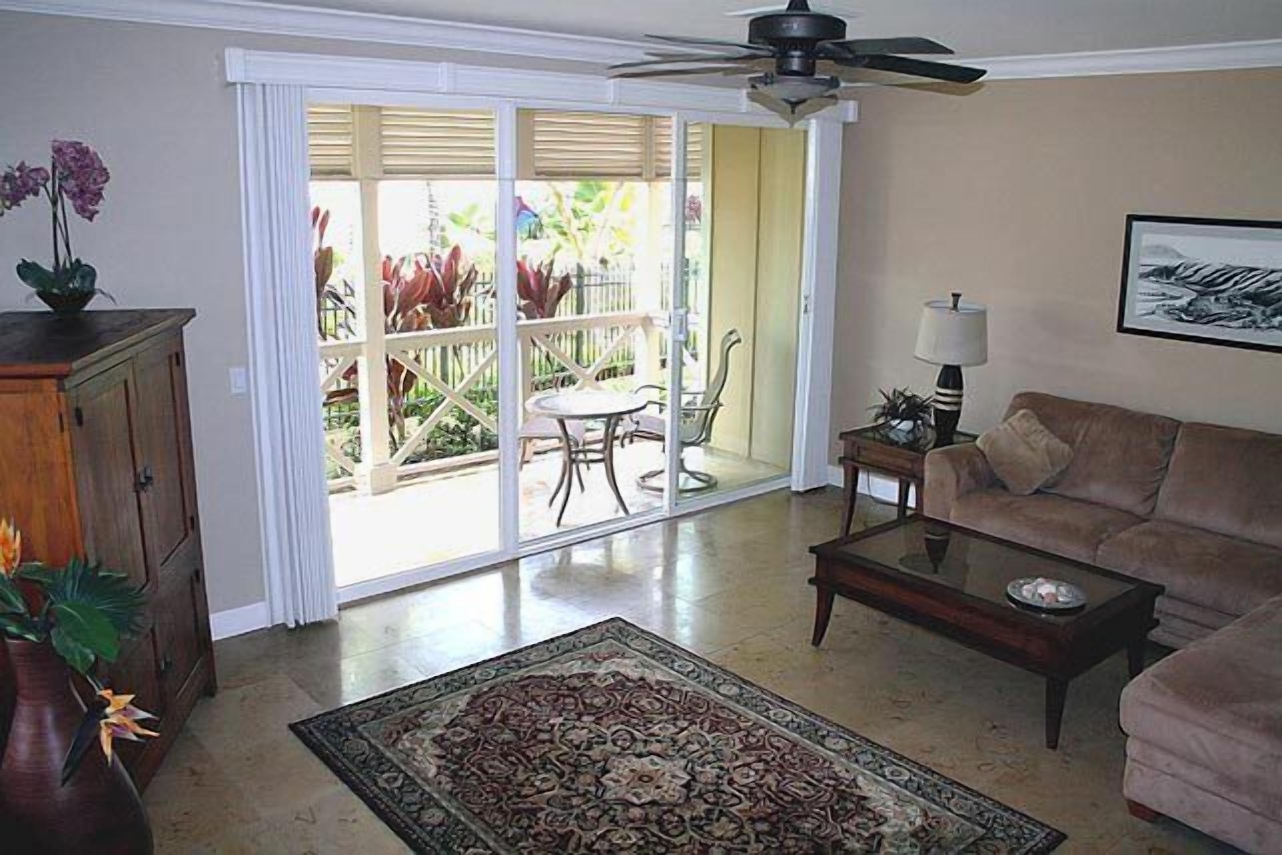 Una sala de estar con sofá, una mesa de centro y un ventanal de vidrio que da a un patio con mobiliario exterior.
