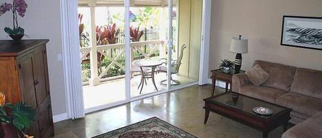 Una sala de estar con sofá, una mesa de centro y un ventanal de vidrio que da a un patio con mobiliario exterior.