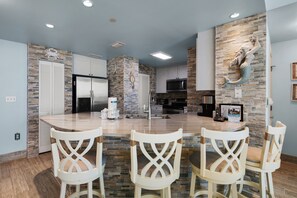 Cocina moderna con salpicadero de piedra, armarios blancos y una isla central con taburetes de bar.