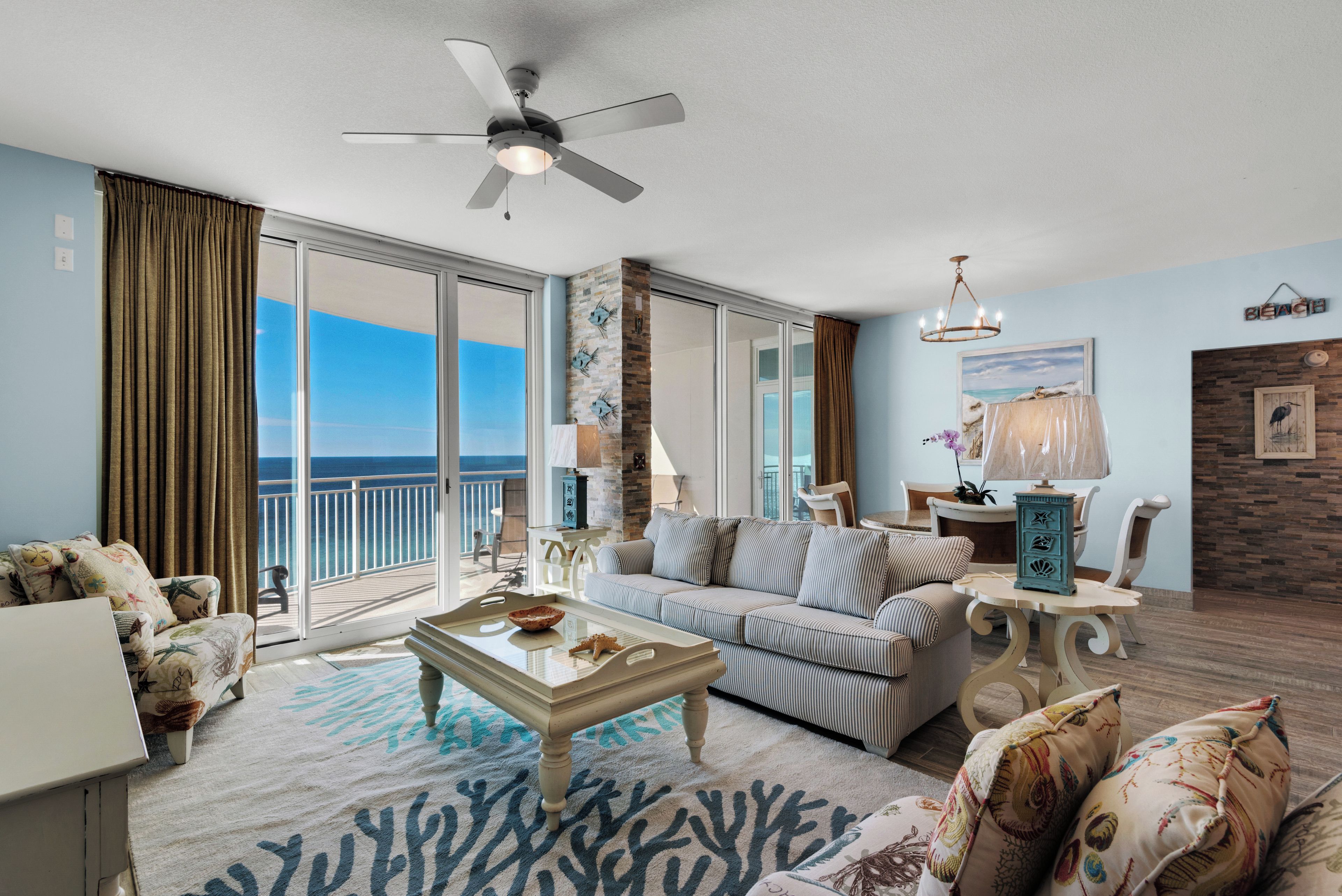 A spacious living room with a large window, a ceiling fan, and a view of the ocean.