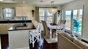 A modern kitchen with a central island, white cabinetry, and a dining area with a table and chairs. - BEACHFRONT 1st Fl Walkout, Crystal Beach, Water Views, FREE Beach Setup, Pool/HotTub - Emerald Dunes (Destin)