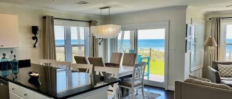 A spacious kitchen with a large island, white cabinetry, and a view of the ocean through the sliding glass doors.