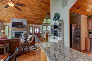 A spacious living room with a stone fireplace, wooden ceiling, and a large TV.