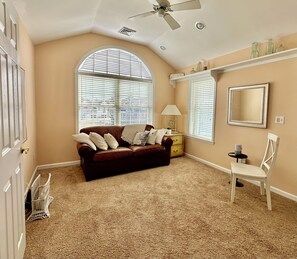 A room with a brown leather sofa, a white chair, a small table, and a ceiling fan.