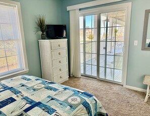 A bedroom with a bed, a television on a cabinet, and a sliding glass door leading to a balcony.
