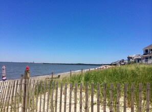 A beach with a wooden fence, a pier in the distance, and buildings on the right.