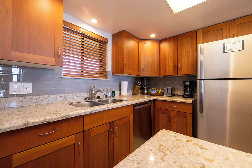 Una cocina con armarios de madera, encimeras de granito, un refrigerador de acero inoxidable y una ventana con persianas.