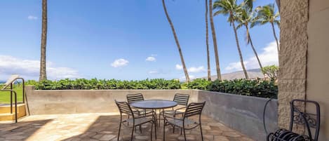 An outdoor patio with a stone floor, a round table with chairs, and a view of palm trees and mountains.