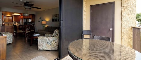 A glass-enclosed balcony with wicker furniture, a door, and a view of the kitchen and living area.