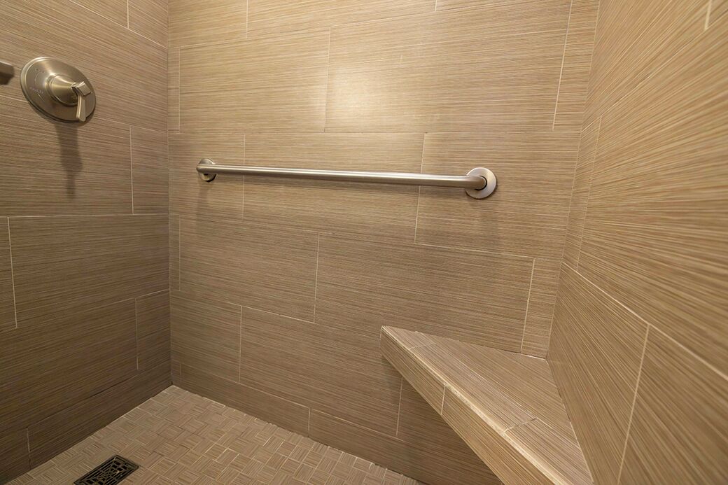 A bathroom with beige tiles, a handrail, and a shower drain.