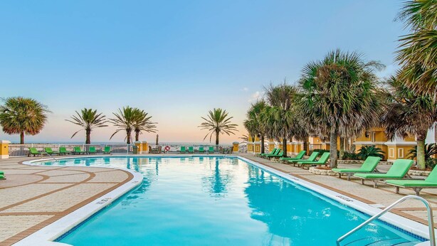 A swimming pool with green lounge chairs and palm trees. - 101 West - Beachfront 3BR/3BA Corner Condo! (Gulf Shores)