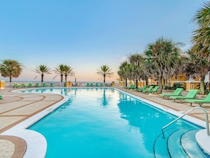 A pool area with green lounge chairs and palm trees, surrounded by a white fence.