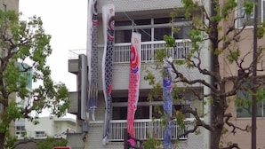 A multi-story building with a balcony decorated with colorful flags. - Next International Homestay (Takamatsu)