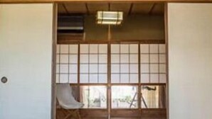 A traditional Japanese room with tatami flooring, a low wooden bed, sliding doors, and a view of the outdoors. - Next International Homestay (Takamatsu)