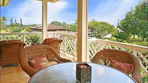 Un espace extérieur aménagé, abrité et doté de meubles en osier et d’une table en verre, offrant une vue sur un paysage luxuriant, avec des arbres et un bâtiment situé au loin.