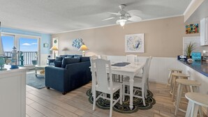 Een ruime woonkamer met een blauwe bank, een witte eettafel en een plafondventilator.