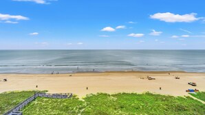 Een strand met een houten vogelzangpad dat naar het water leidt, een zandstrand en een heldere lucht.